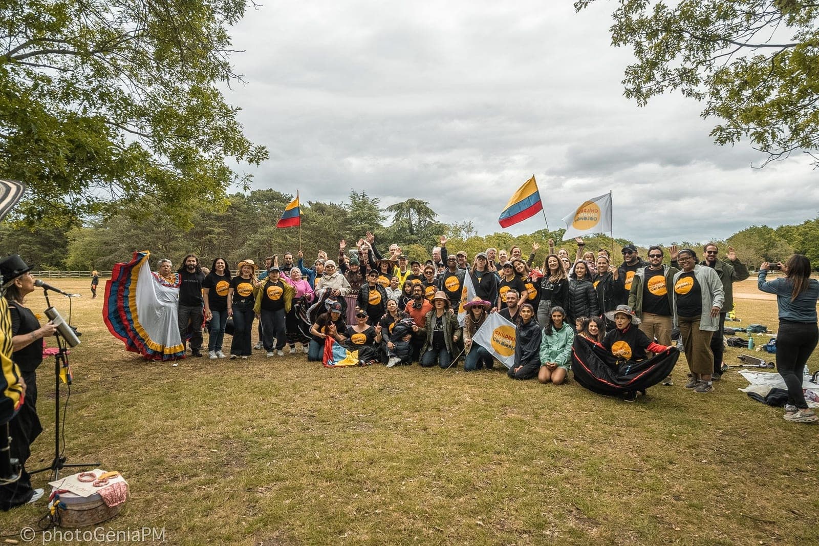 Foto de grupo del Thames Walk 2026 en un parque: decenas de personas con camisetas de CCC, banderas de Colombia y una bailarina con falda tricolor