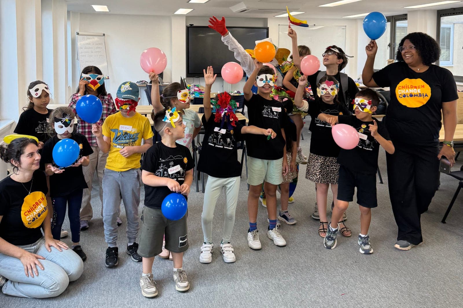 Niños del campamento de verano de Colombia Colores con antifaces y globos de colores, junto a dos monitoras de Children Change Colombia