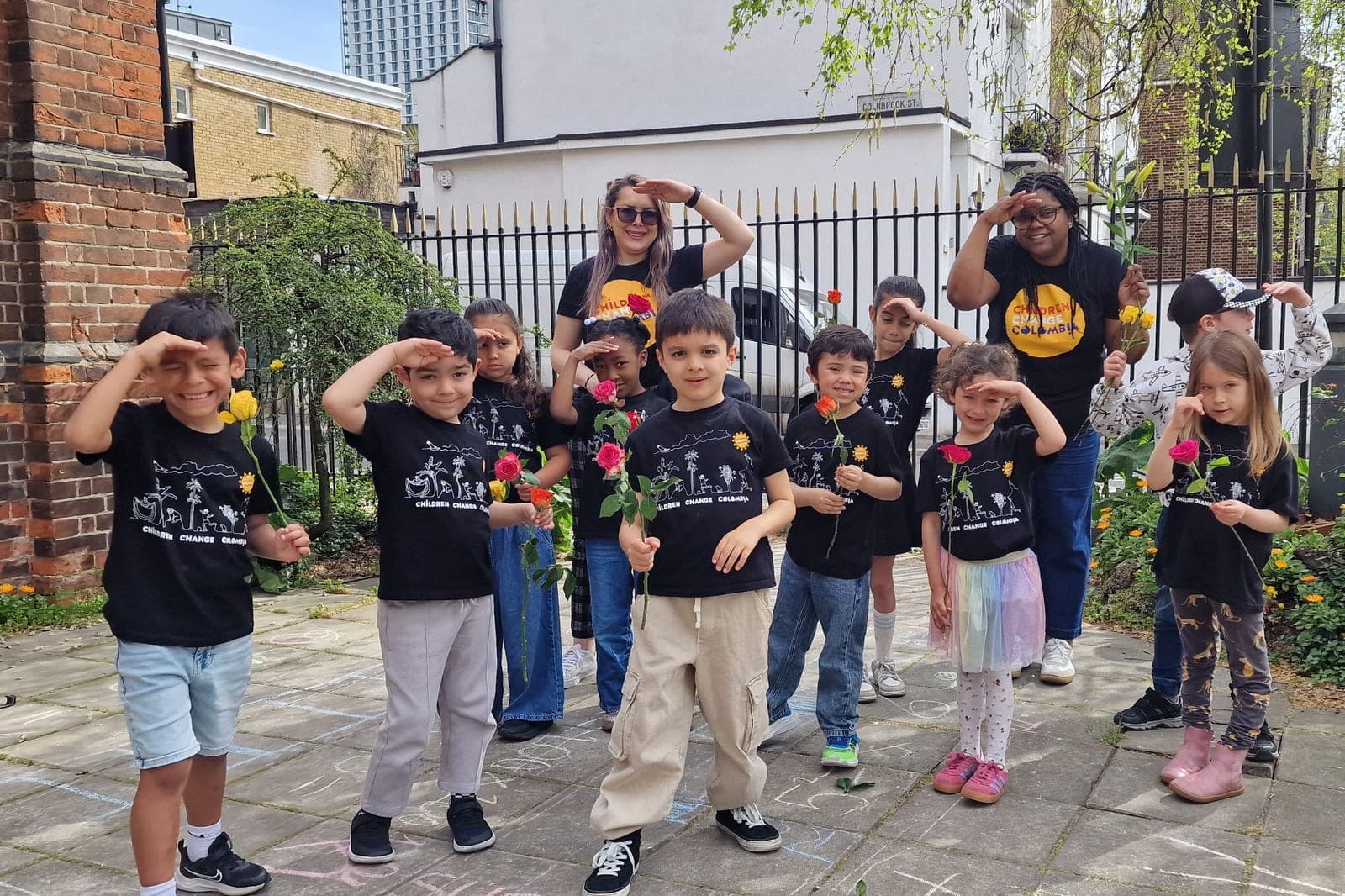 Niños de Colombia Colores con camisetas de Children Change Colombia y una rosa en la mano posan con dos profesoras, haciendo visera con la mano