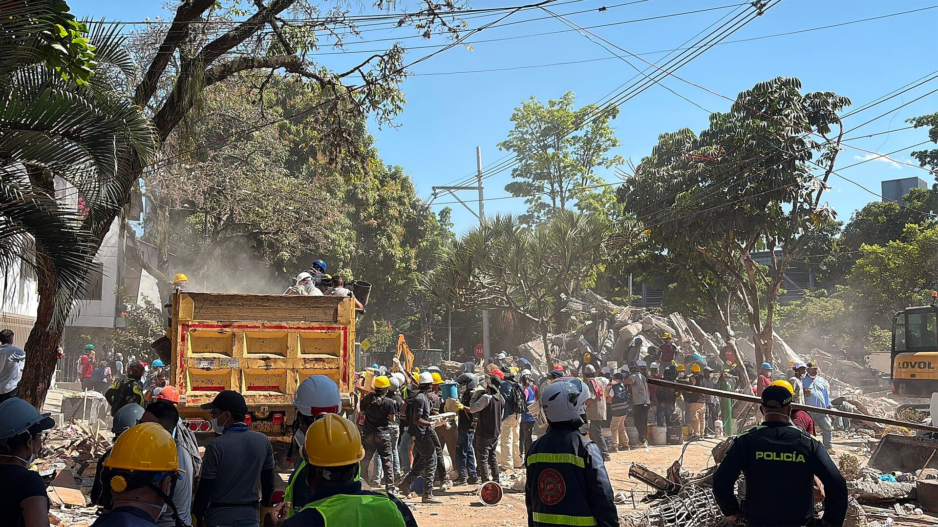 Decenas de trabajadores con cascos, policías y voluntarios trabajan juntos entre los escombros en Cali